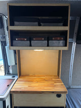 RV rental interior: Organized wooden cabinets, bright countertop lighting, and fabric storage bins in a compact camper kitchen.