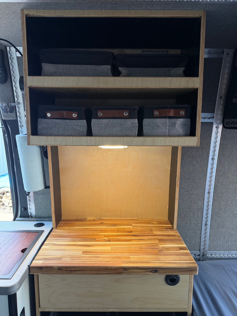 RV rental interior: Organized wooden cabinets, bright countertop lighting, and fabric storage bins in a compact camper kitchen. — photo 12