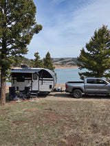 Beautiful **rv rental** setup: GMC truck towing a Go Lite travel trailer by a serene lake and mountains, ideal for camping.