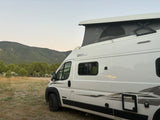 White pop-top RV rental in a mountain landscape, ready for off-grid adventure. Ideal for nature travel.