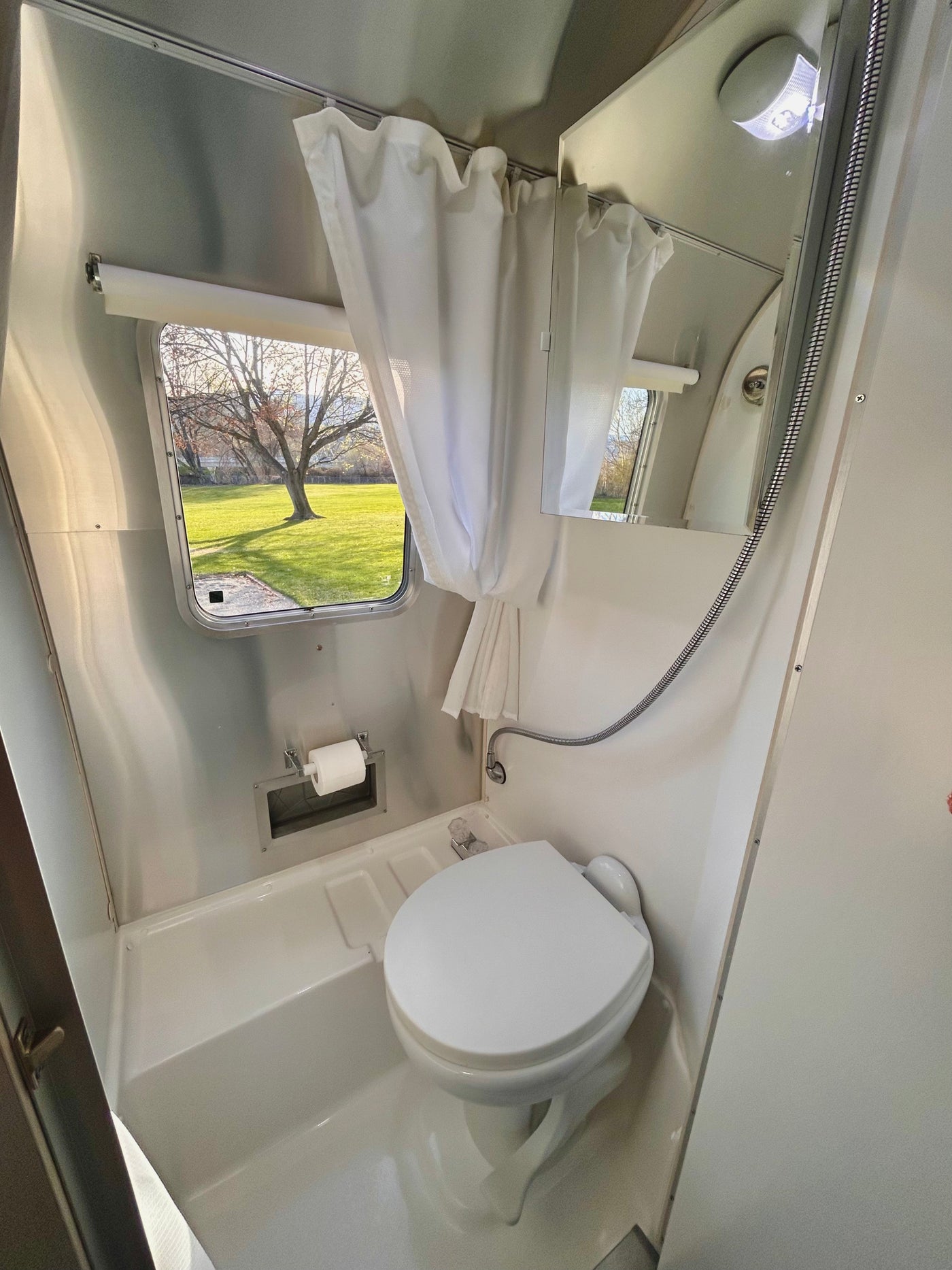 Compact RV rental wet bath with toilet, shower, and outside window view, perfect for travel trailer adventures. — photo 14