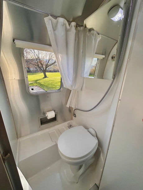 Compact RV rental wet bath with toilet, shower, and outside window view, perfect for travel trailer adventures.