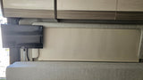 RV rental interior showing a small TV, two-tone cabinets, upholstered wall, and a pulled-down window shade over comfortable seating.