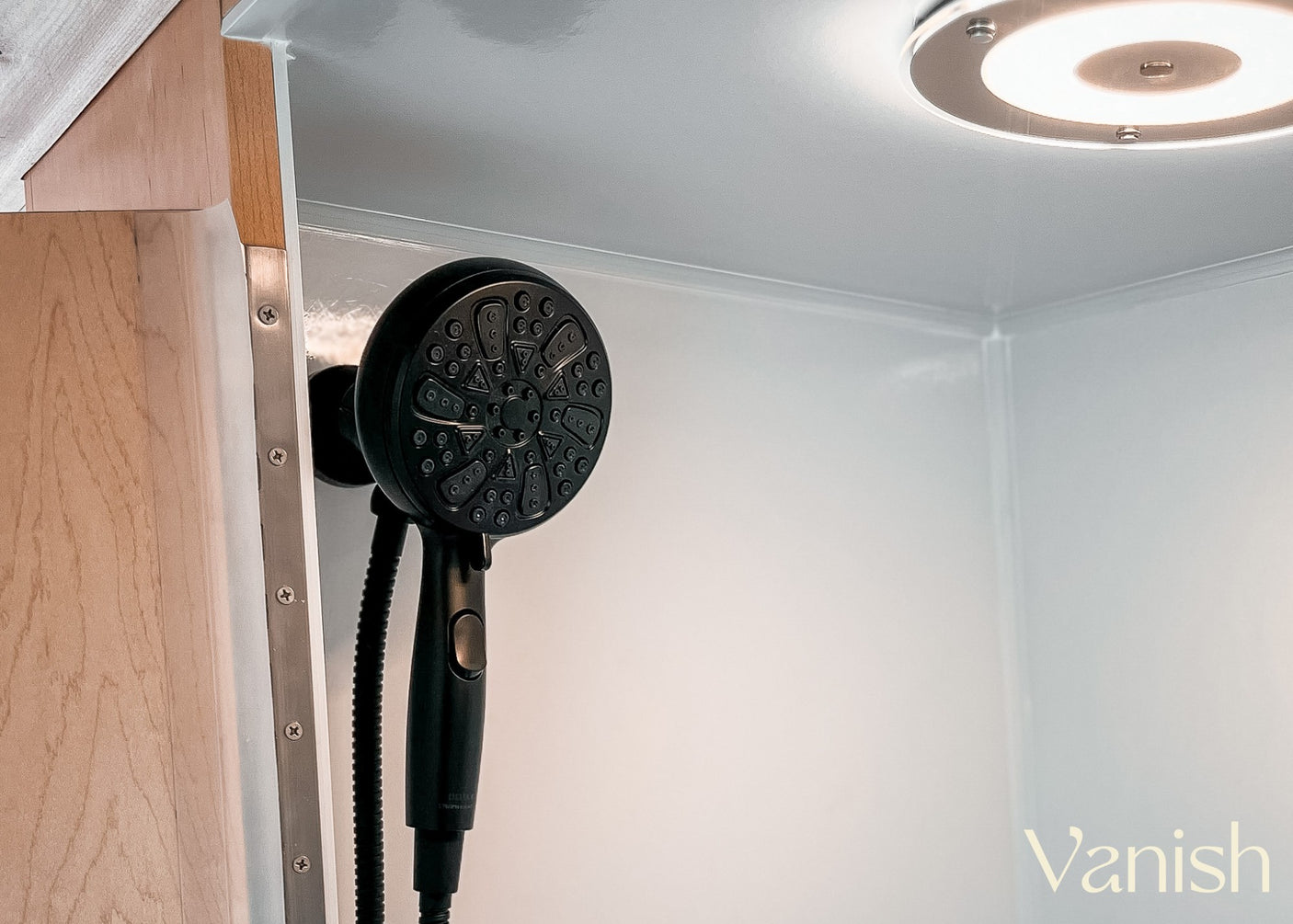 Inside an RV rental: a modern, compact shower stall with a black shower head and bright ceiling light, ideal for travel.