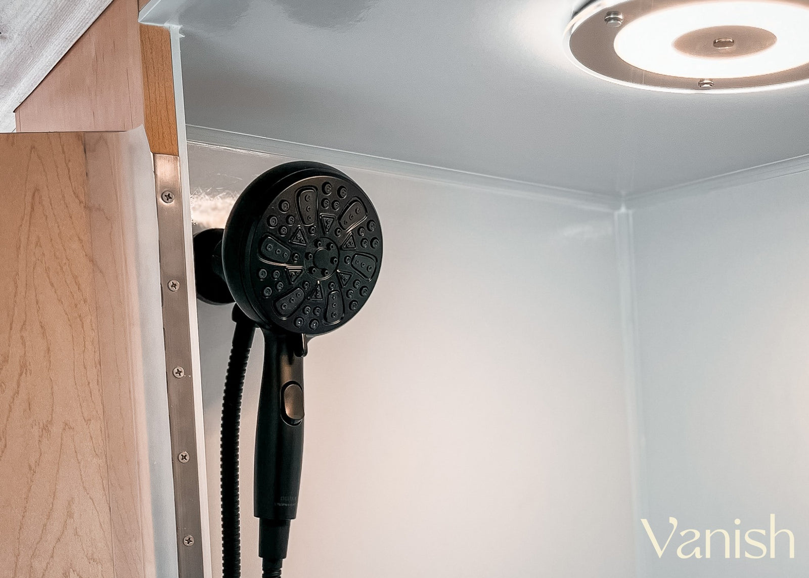 Inside an RV rental: a modern, compact shower stall with a black shower head and bright ceiling light, ideal for travel.