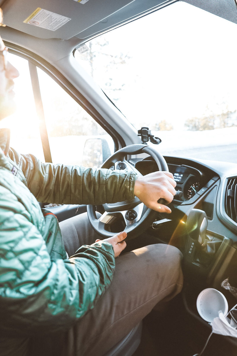 Inside an RV rental, a person in a green jacket drives, hands on the wheel. Bright sun illuminates the interior winter scene. — photo 7
