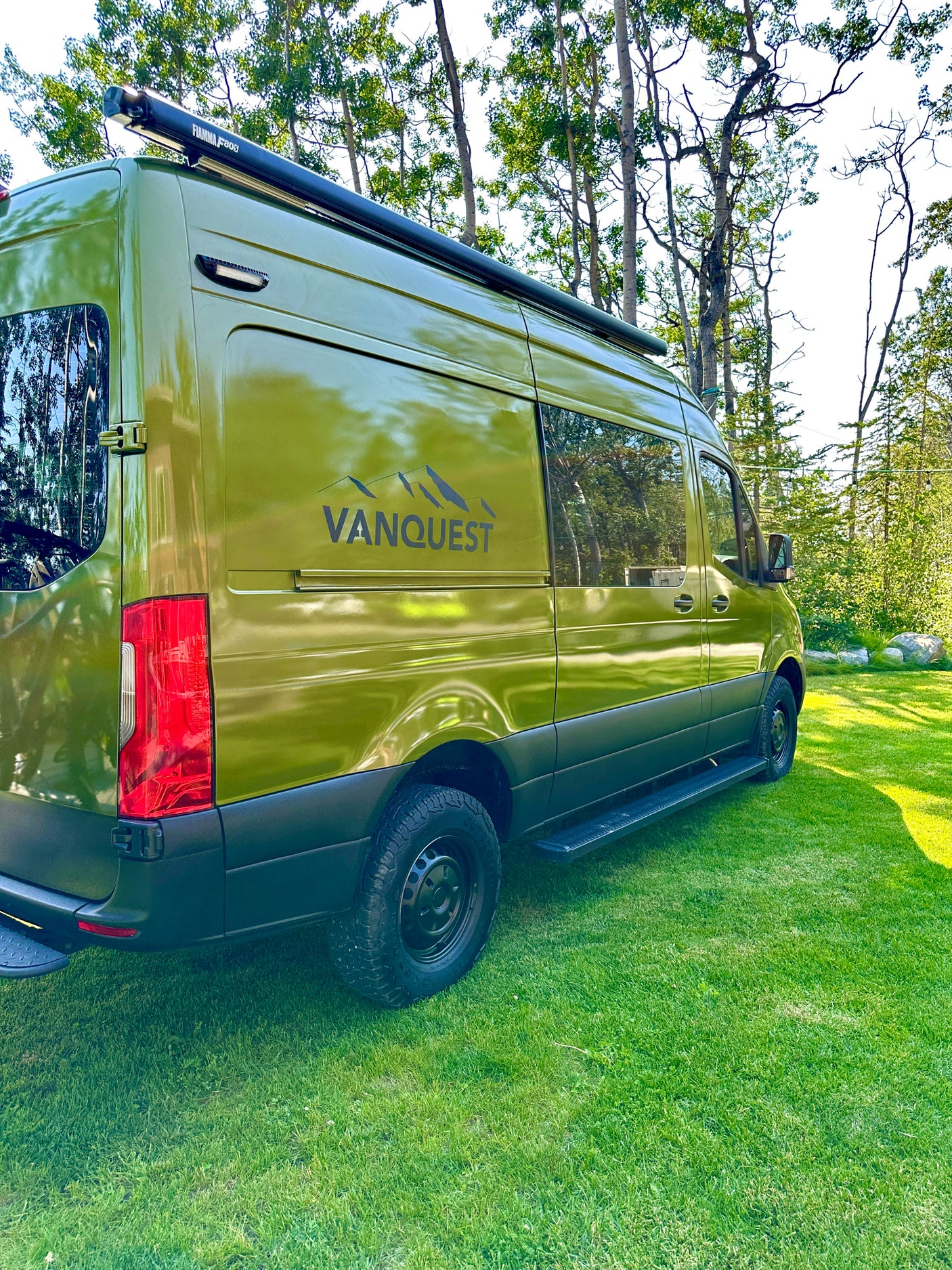 Green camper van RV rental by VANQUEST parked on grass, ideal for outdoor adventures.