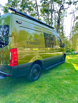 Green camper van RV rental by VANQUEST parked on grass, ideal for outdoor adventures.