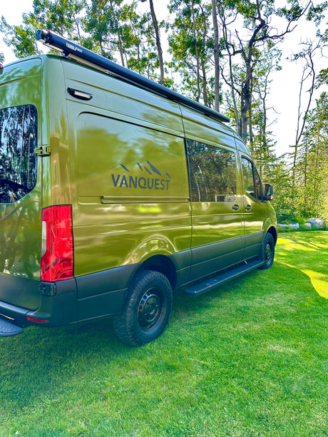 Green camper van RV rental by VANQUEST parked on grass, ideal for outdoor adventures.