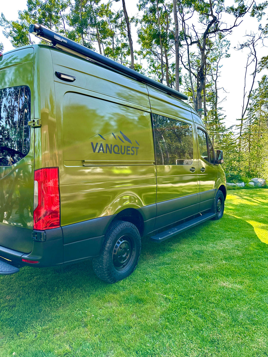 Green camper van RV rental by VANQUEST parked on grass, ideal for outdoor adventures.