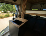 Step into this sleek RV rental! Features a modern kitchen with sink, comfy bed, and a beautiful outdoor view from the open door.