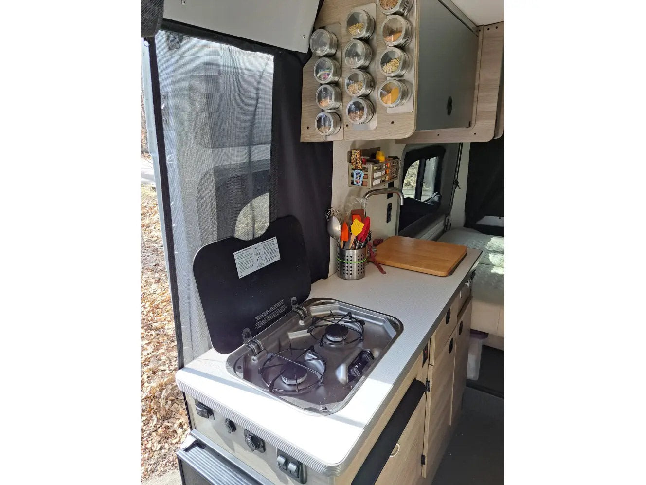 Compact RV rental kitchen with a stove, sink, spice rack, and cooking essentials. Perfect for road trip meals.