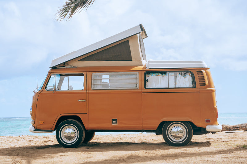 An iconic orange vintage VW Bus RV rental parked on a sunny beach with the ocean waves in the background. — photo 2