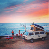 RV rental dream: White camper van with surfboards parked beachfront at stunning sunset. Couple enjoys ocean view.