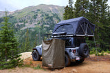 An RV rental Jeep Wrangler, equipped with a rooftop tent and privacy enclosure, parked for camping in a scenic mountain forest.