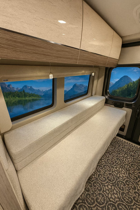 Modern **rv rental** interior with plush bench seating, overhead storage, and large windows revealing a mountain lake view.