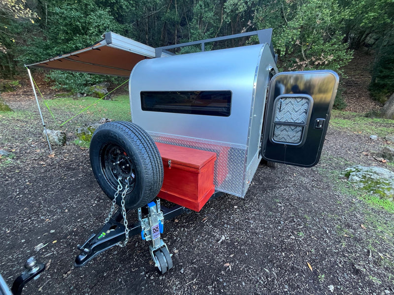  and side awning for camping comfort.|Small silver teardrop RV rental with an extended awning at a woodsy campsite — photo 13