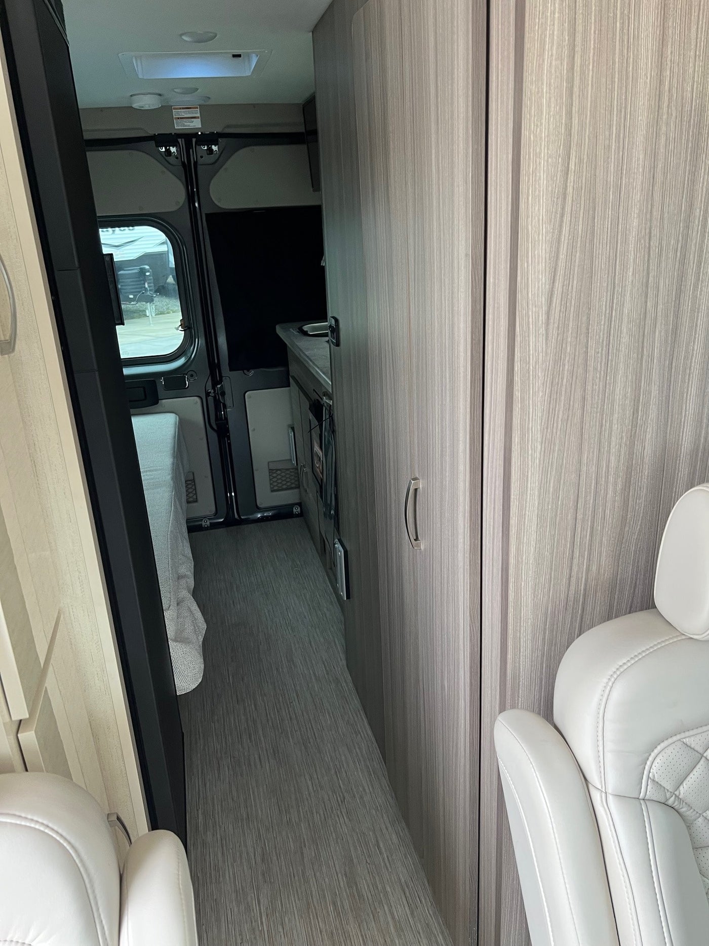 Inside a modern **rv rental**, looking towards the rear. Features a light-toned interior with a bed, galley, & captains chair. — photo 4
