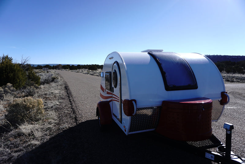 This white teardrop camper RV rental is ready for adventure on a desert road under a clear blue sky. — photo 6