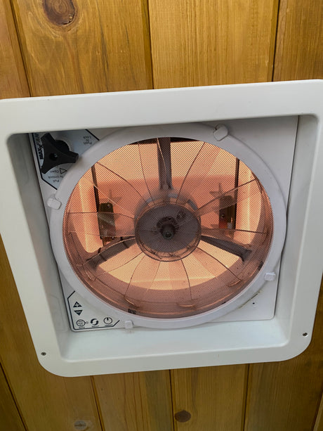 Inside an RV rental: a MaxxAir roof vent fan with its control panel and mesh screen, installed in a wooden ceiling.