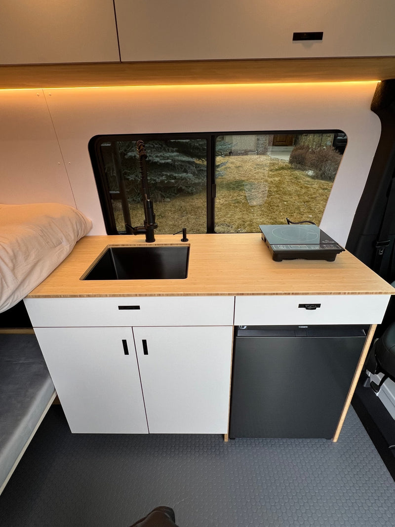 Modern RV rental kitchenette: bamboo counter, black sink, induction cooktop, Dometic fridge, and cabinets. — photo 13