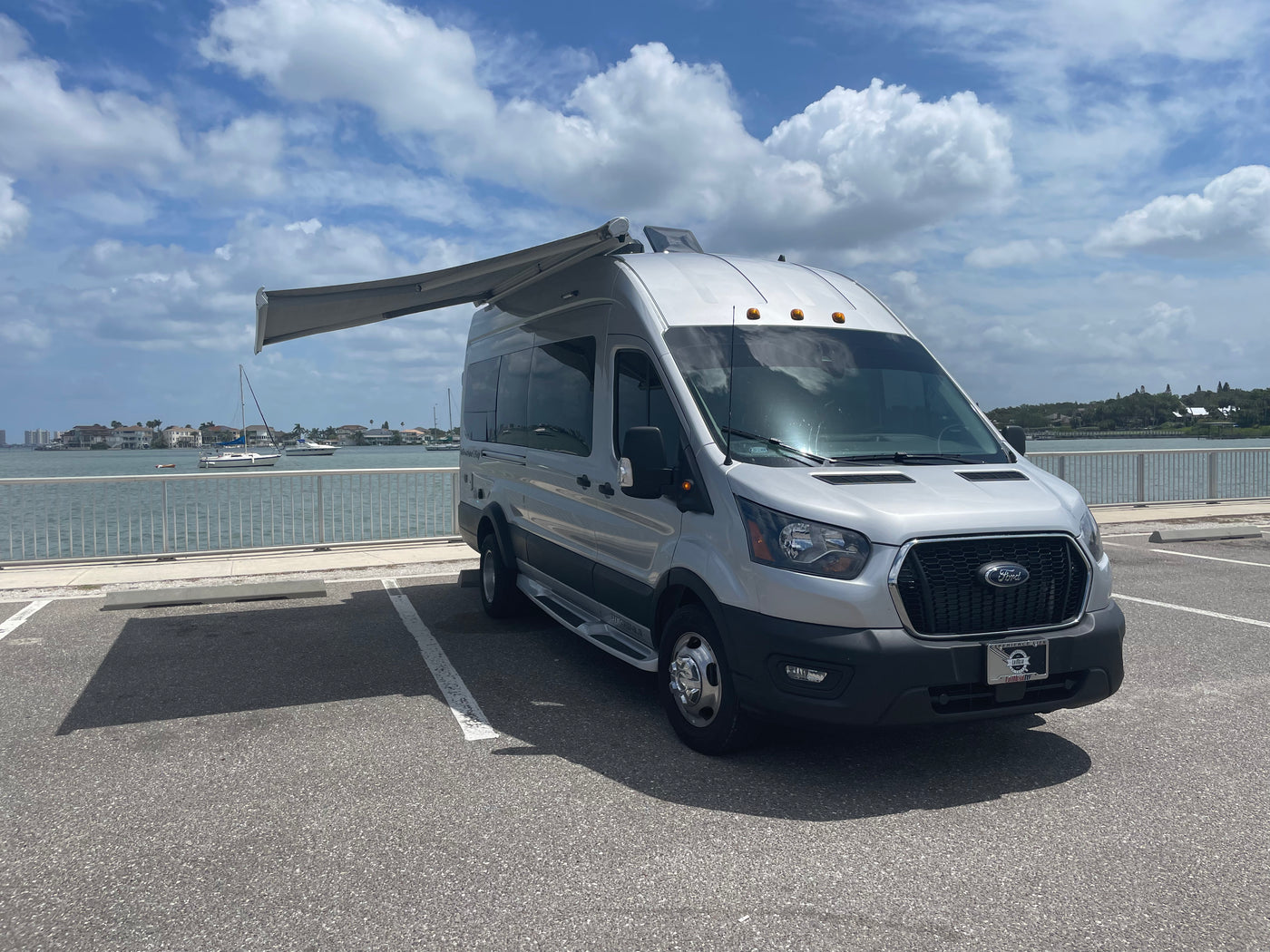 Silver Ford Transit camper van RV rental with extended awning, parked at a waterfront. — photo 7