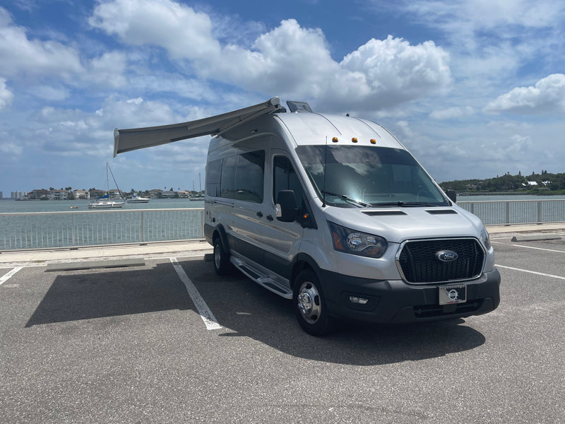 Silver Ford Transit camper van RV rental with extended awning, parked at a waterfront. — photo 7