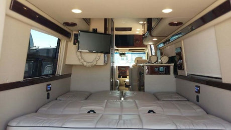 Luxurious RV rental interior shows a spacious bed, multiple TVs, and a clear view to the front cabin for comfortable travel.