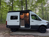 Enjoying an RV rental adventure. A Tiffin camper van with its door open, showing a woman inside working, parked in a forest.