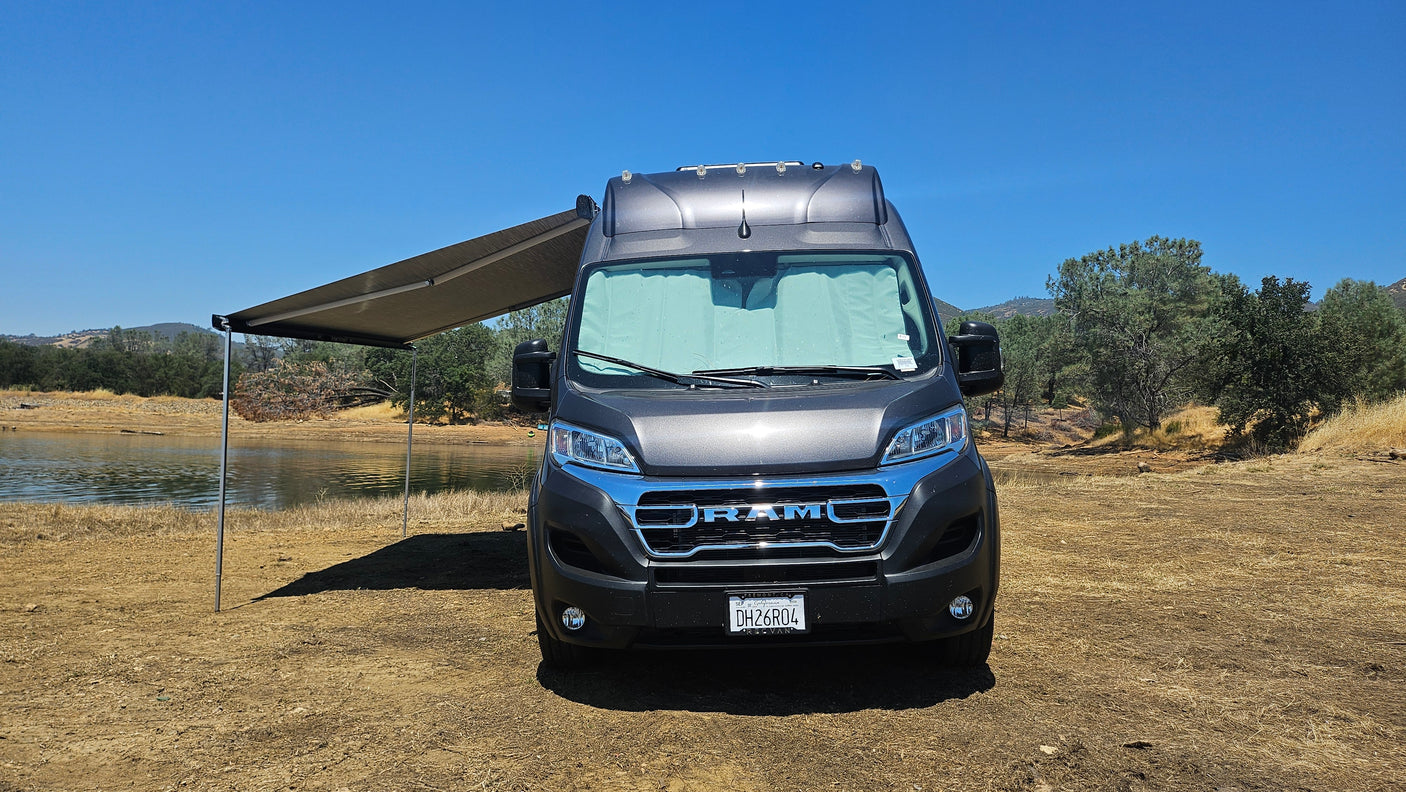 This grey RV rental, with its awning extended, is perfectly parked by a tranquil lake for a scenic camping adventure.