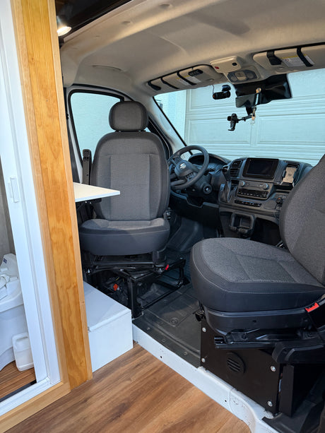 RV rental interior: Front cabin with swiveling driver's seat, dashboard, and attached table. Modern tech & wood accents for comfy travel.