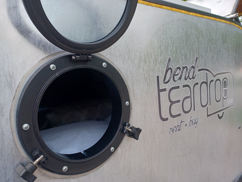 Side view of a Bend Teardrop RV rental with its round window open, revealing a cozy bed inside. — photo 13