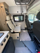 RV rental interior: cream quilted rear seats, black front seats, kitchenette, control panel, and overhead storage.