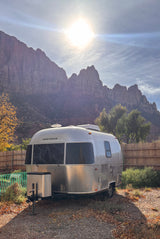 Experience nature with this Airstream rv rental! Silver travel trailer nestled at the base of majestic mountains under a bright, sunny sky.