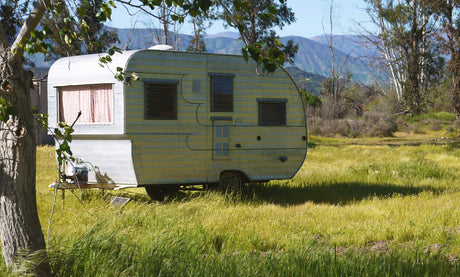 Rustic RV rental parked in a sun-drenched field with distant mountains. An ideal vintage travel trailer for peaceful escapes.