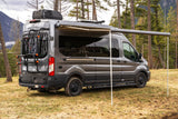 Modern gray rv rental van, "Sanctuary" model, with awning extended and bike rack, nestled in a scenic mountain forest.