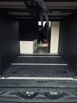 Interior of an RV rental's rear cargo space: dark, textured walls/floor, aluminum tie-down tracks, and a white storage box.