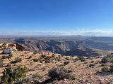 White RV rental parked at a desert canyon overlook, showcasing stunning layered rock formations & distant mesas under a blue sky.