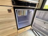 View of an open, compact Isotherm refrigerator inside an RV rental. It has a freezer & wire shelves within light wood cabinets.