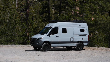 Sleek gray Mercedes-Benz Sprinter RV rental parked on a forest dirt road, perfect for outdoor adventure & exploration.