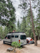 Serene forest RV rental camping: a Sprinter van, tent, & people relaxing on the van's roof.