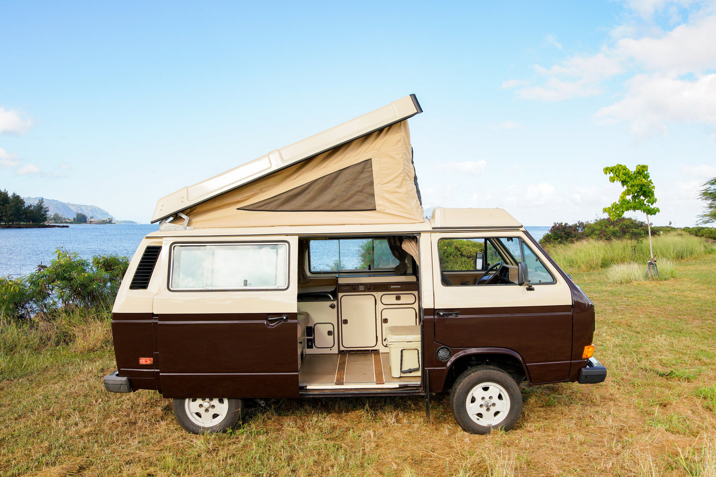 Two-tone Westfalia camper van RV rental, pop-top open, parked by a scenic bay. Adventure awaits!