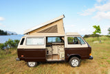 Two-tone Westfalia camper van RV rental, pop-top open, parked by a scenic bay. Adventure awaits!