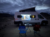 An rv rental camper van displays a power bank ad projected on its side, watched by a person camping under snowy mountains.