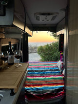 RV rental: Sunset ocean view from a cozy interior with wine and a colorful blanket.