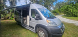 Experience nature with this silver camper van rv rental, featuring an open door, extended awning, and a view of its cozy interior.