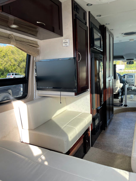 Spacious RV rental interior with TV, cream seating, dark wood cabinets, and appliances like a refrigerator.