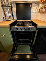 This compact RV rental kitchen features an open oven, gas cooktop, and stainless steel water filter, ready for your road trip meals.