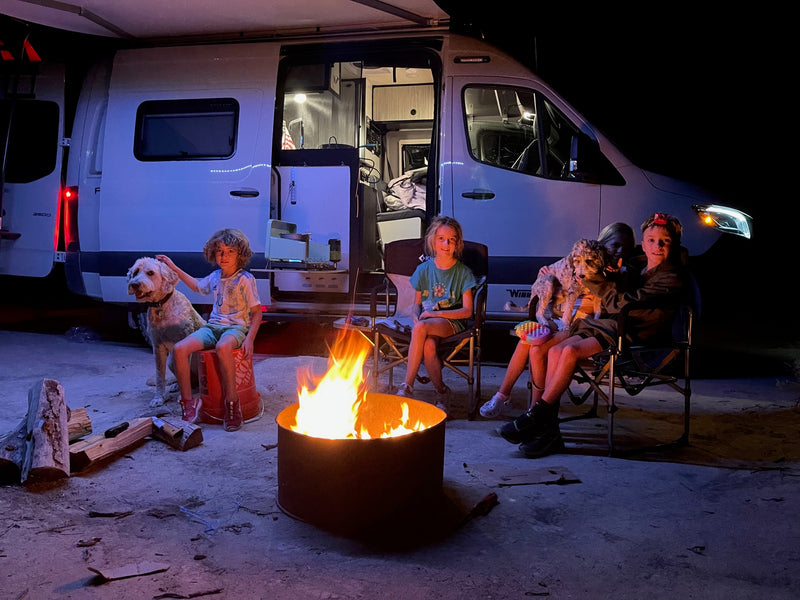 Family and dogs enjoy a warm campfire beside their RV rental at night, creating cherished camping memories. — photo 2