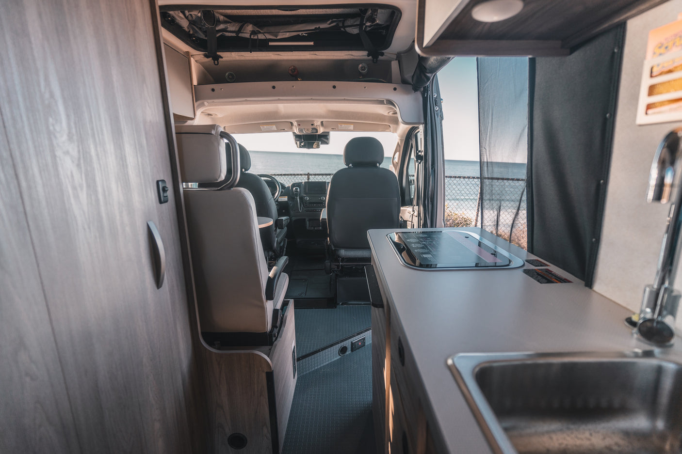 Inside a modern rv rental with a kitchenette, cozy front seats, and a serene ocean view visible through the windshield.